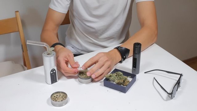 guy puts cannabis into a glass tube for use through a vaporizer