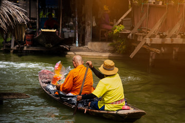 Obraz premium floating Dawning, Thai monk paddle the boat receiving food on canal The tradition of making merit to monks morning