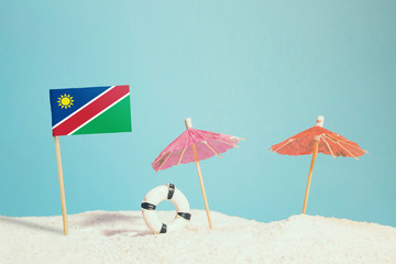 Fototapeta premium Miniature flag of Namibia on beach with colorful umbrellas and life preserver. Travel concept, summer theme.