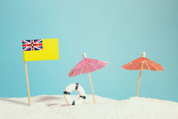 Miniature flag of Niue on beach with colorful umbrellas and life preserver. Travel concept, summer theme.