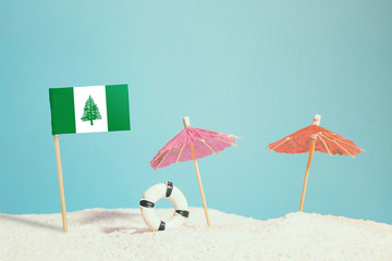 Fototapeta na wymiar Miniature flag of Norfolk Island on beach with colorful umbrellas and life preserver. Travel concept, summer theme.