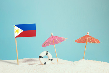 Miniature flag of Philippines on beach with colorful umbrellas and life preserver. Travel concept, summer theme.