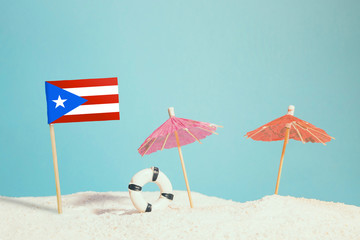 Miniature flag of Puerto Rico on beach with colorful umbrellas and life preserver. Travel concept, summer theme.