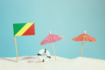 Miniature flag of Republic Of The Congo on beach with colorful umbrellas and life preserver. Travel concept, summer theme.