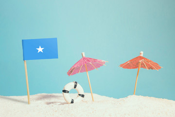 Miniature flag of Somalia on beach with colorful umbrellas and life preserver. Travel concept, summer theme.