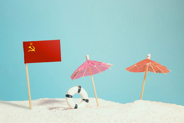 Miniature flag of Soviet Union on beach with colorful umbrellas and life preserver. Travel concept, summer theme.
