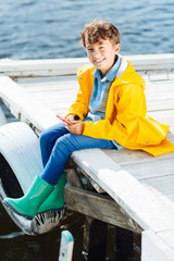 Beaming boy sitting near river wearing raincoat