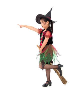 Little girl asian in witch costume, her hand is holding the .broom while standing and pointing to the front. Halloween concept.