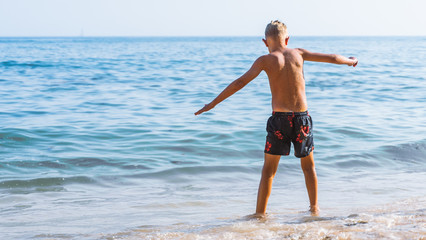 Fototapeta na wymiar caucasian boy jumping in sea waves at the beach. kids fun at vacation time. travel with children