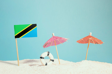 Miniature flag of Tanzania on beach with colorful umbrellas and life preserver. Travel concept, summer theme.