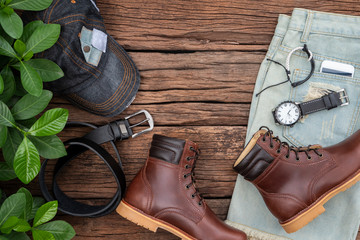 Men's accessories and essential travel items with space for text or object on rustic wooden background. All leather include brown boots, belt, phone, hat, sunglass, short and watch. Flat lay, top view