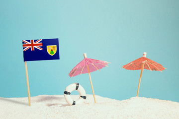 Miniature flag of Turks And Caicos Islands on beach with colorful umbrellas and life preserver. Travel concept, summer theme.