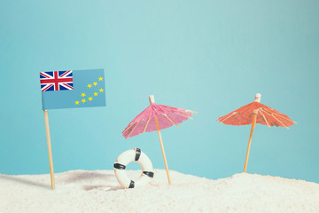 Miniature flag of Tuvalu on beach with colorful umbrellas and life preserver. Travel concept, summer theme.
