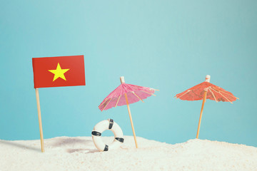 Miniature flag of Vietnam on beach with colorful umbrellas and life preserver. Travel concept, summer theme.