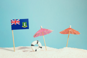 Miniature flag of British Virgin Islands on beach with colorful umbrellas and life preserver. Travel concept, summer theme.