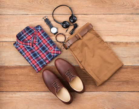 Flat lay, top view, men fashion casual clothing set on wooden background include brown derby shoes, yellow pants, belt ,watch, sunglass, earphone, bracelet and office shirt.