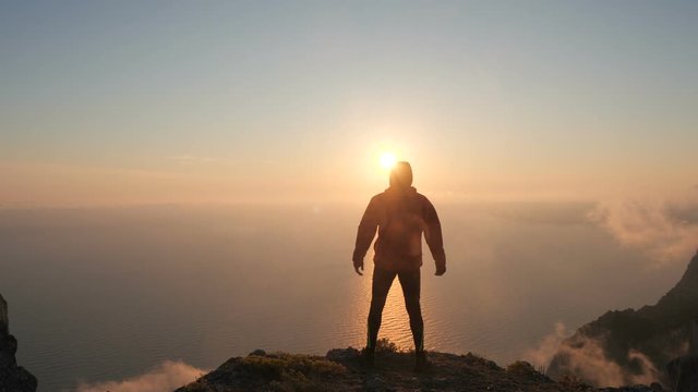 Silhuette of Young man arms outstretched observing beautiful dramatic colorful sunset above a sea from a high mountain in Crimea.