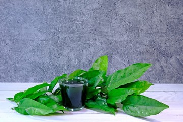 Fresh organic Bai Ya Nang (Tiliacora Triandra, Yanang) juice in a glass on white table decorated...