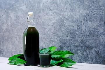Fresh organic Bai Ya Nang (Tiliacora Triandra, Yanang) juice cold press by hand in the bottle on white table and cement background.