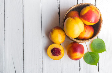 Delicious peaches in basket on white wooden table
