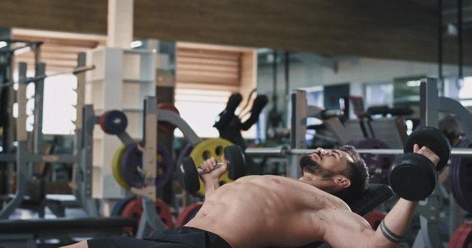 At an athletic gym a handsome guy is doing weights as he is working on a fitter body