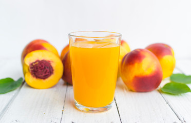 Delicious and juicy peach (nectarina) with glass of juice on white wooden table