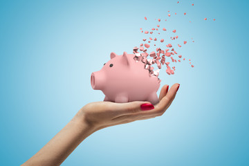 Close-up of woman's hand facing up and holding cute pink piggy bank that has started to...