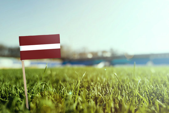 Miniature stick Latvia flag on green grass, close up sunny field. Stadium background, copy space for text.