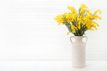Blossom of Mimosa flower in ceramic vase on white wooden background with space for text