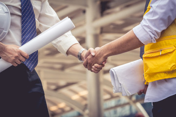 Close up of  businessman's hands are shaking hands over a deal. Their hands carry blueprint and...