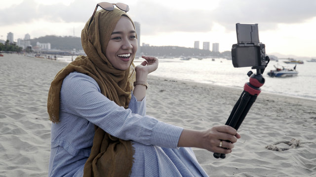 Blogger Asian Muslim woman record vlog video on beach, young beautiful female happy to using phone making video vlog