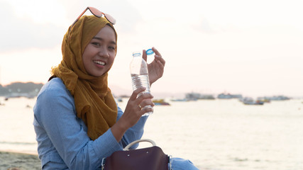 portrait of young muslim asia woman with hijab and blue dress holding and opening a mineral water bottle