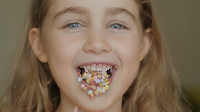 A child is smiling with a mouth full of candy. Little girl eating candy. Child eating chicle. Close up portrait silly girl with wavy hair sticking out tongue shaped candy pieces on tip.