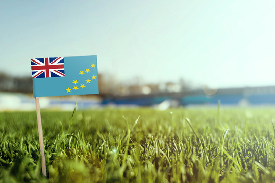 Miniature stick Tuvalu flag on green grass, close up sunny field. Stadium background, copy space for text.
