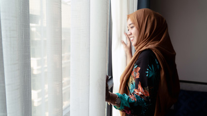 portrait of hijab Woman Standing By Bedroom Window And Opening Curtains