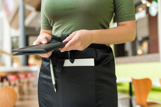 Cropped image of woman waitress in apron hold out bill folder to cafe visitor of cafe or restaurant.