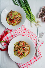 Hot salad with chicken, zucchini and chili pepper, sprinkled with sesame seeds and herbs. Asian food. White wood background.