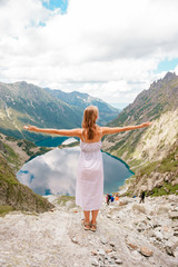 Beautiful long haired girl in white dress standing with hands apart in Polish mountains with fabulous scenic view on background