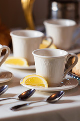 Tea cup sitting on a saucer with a lemon wedge.