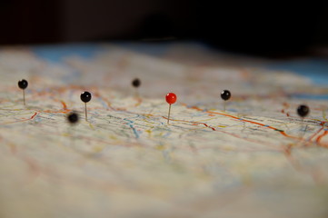 closeup of pin sticks into a real map. travelling to. pin marking location on map. maps navigation with red and black color point markers design background.