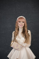Obraz premium beautiful blonde girl in a beige dress sitting on a chair and looking at the camera with a smile on a gray textural background