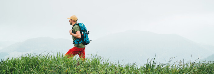 Side shot of hiker man walking by the foggy cloudy weather mountain range path with backpack. Active sport backpacking healthy lifestyle concept. Website header cropping.