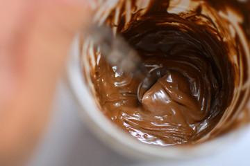 Spoon taking chocolate cream out of the white plastic jar