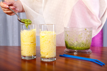 A woman puts kiwi puree into a smoothie glass.