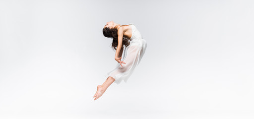 panoramic shot of young ballerina jumping in dance on grey background