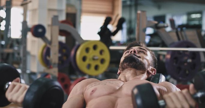 A gym guy is doing heavy lifts while flexing his muscles , and getting them perfect abs