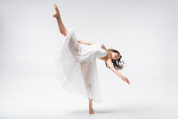 beautiful ballerina in white dress dancing on grey background