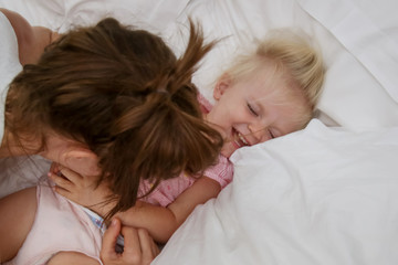 Mother and her infant baby cuddling in the bed, adorable blonde baby and her mum having fun, happy family life concept