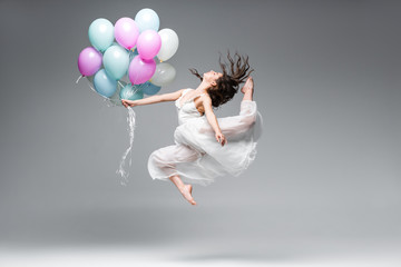 beautiful ballerina in white dress dancing with festive balloons on grey background