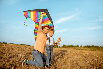 Father with son launching colorful air kite on the field. Concept of a happy family having fun during the summer activity